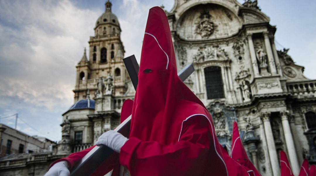 Unos penitentes pasan en procesión por la plaza Belluga de Murcia, frente a la catedral