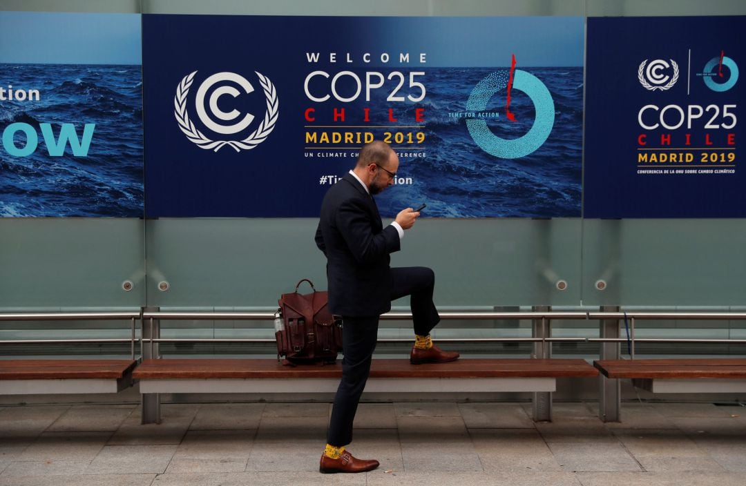 Un hombre mira el móvil delante de un cartel de la COP25 celebrada en Madrid