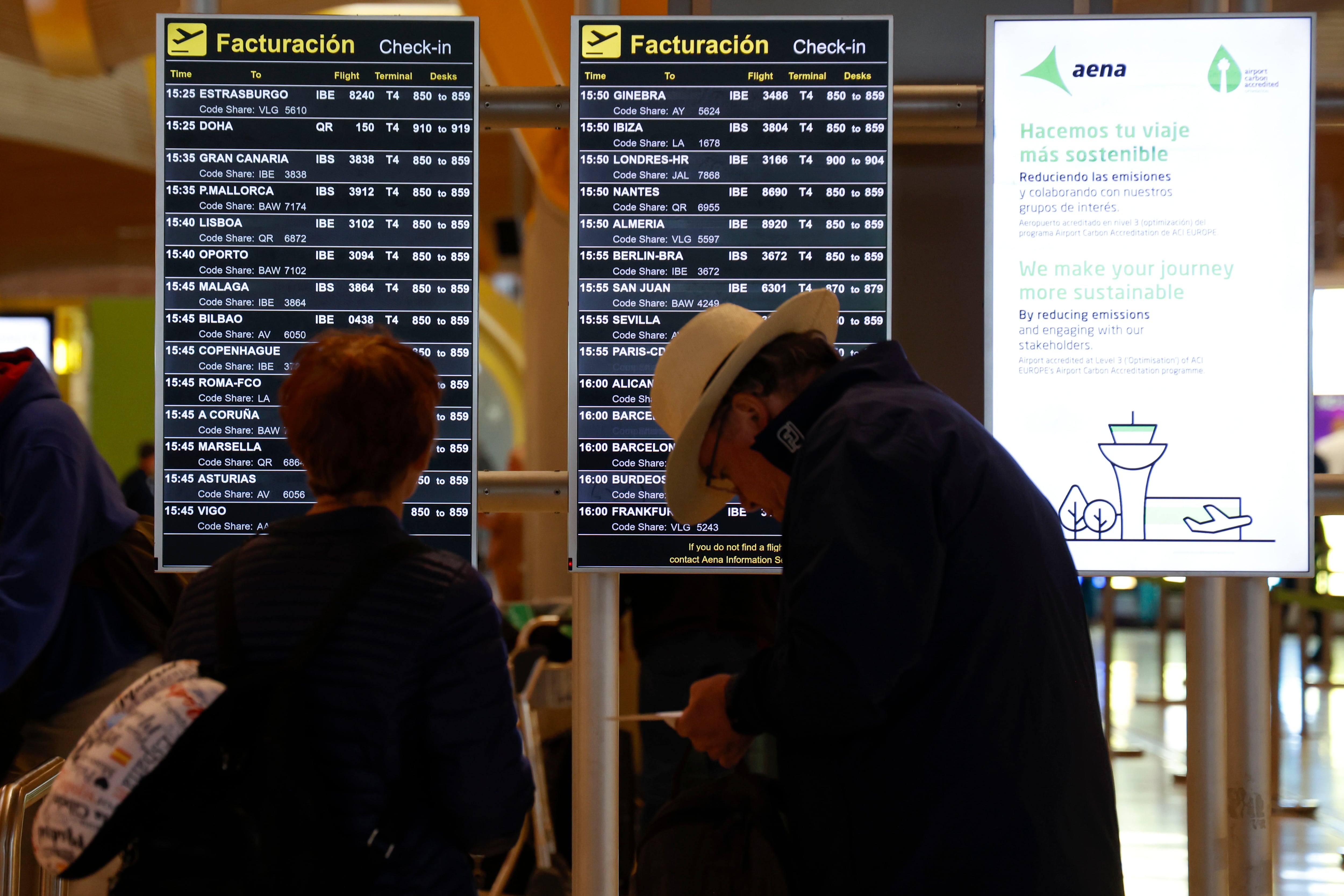 Dos personas revisan el panel informativo del Aeropuerto Adolfo Suárez.