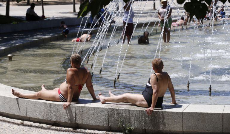 Varias personas se refrescan en una fuente de Madrid Río en una jornada marcada por las altas temperaturas registradas en la capital de España