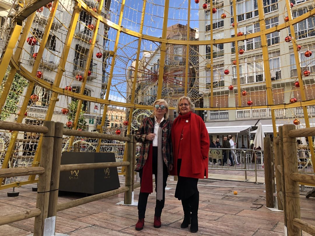 La concejala de Fiestas, Teresa Porras (a la derecha) posa bajo el árbol de navidad en la Plaza de la Constitución acompañada de la presidenta de la asociación de comerciantes Centro Histórico, Juanibel Vera