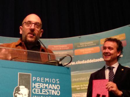 Javier Ajenjo recoge el premio de honor Hermano Celestino bajo la mirada sonriente de Enrique García director de San Gabriel Ciudad de la Educación