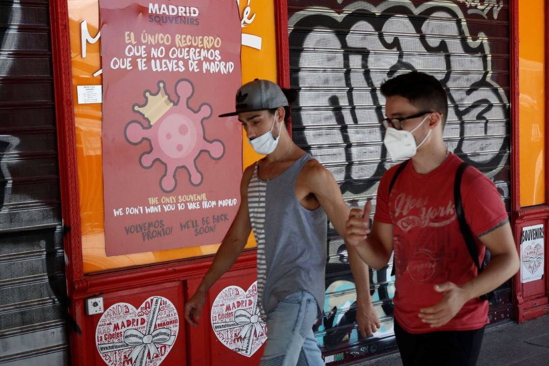 Dos jóvenes pasan ante un cartel alusivo al coronavirus en el centro de Madrid