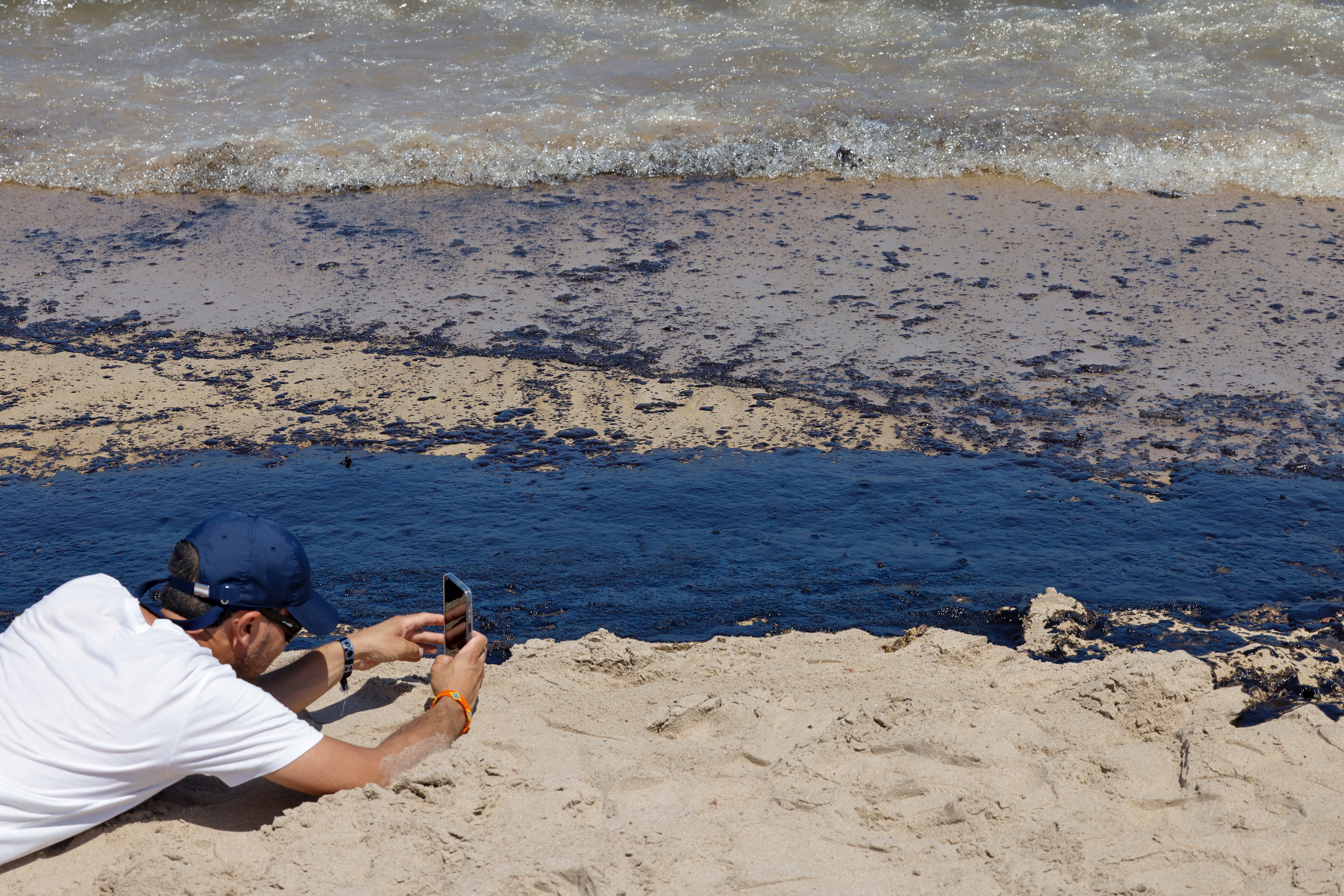 Una persona toma una imagen del vertido de combustible, que según las primeras estimaciones mide entre 1,5 y dos kilómetros, y que ha obligado a prohibir el baño en las playas de l&#039;Arbre del Gos y El Saler, en València, donde se ha puesto la bandera roja, según fuentes municipales y de la Generalitat.