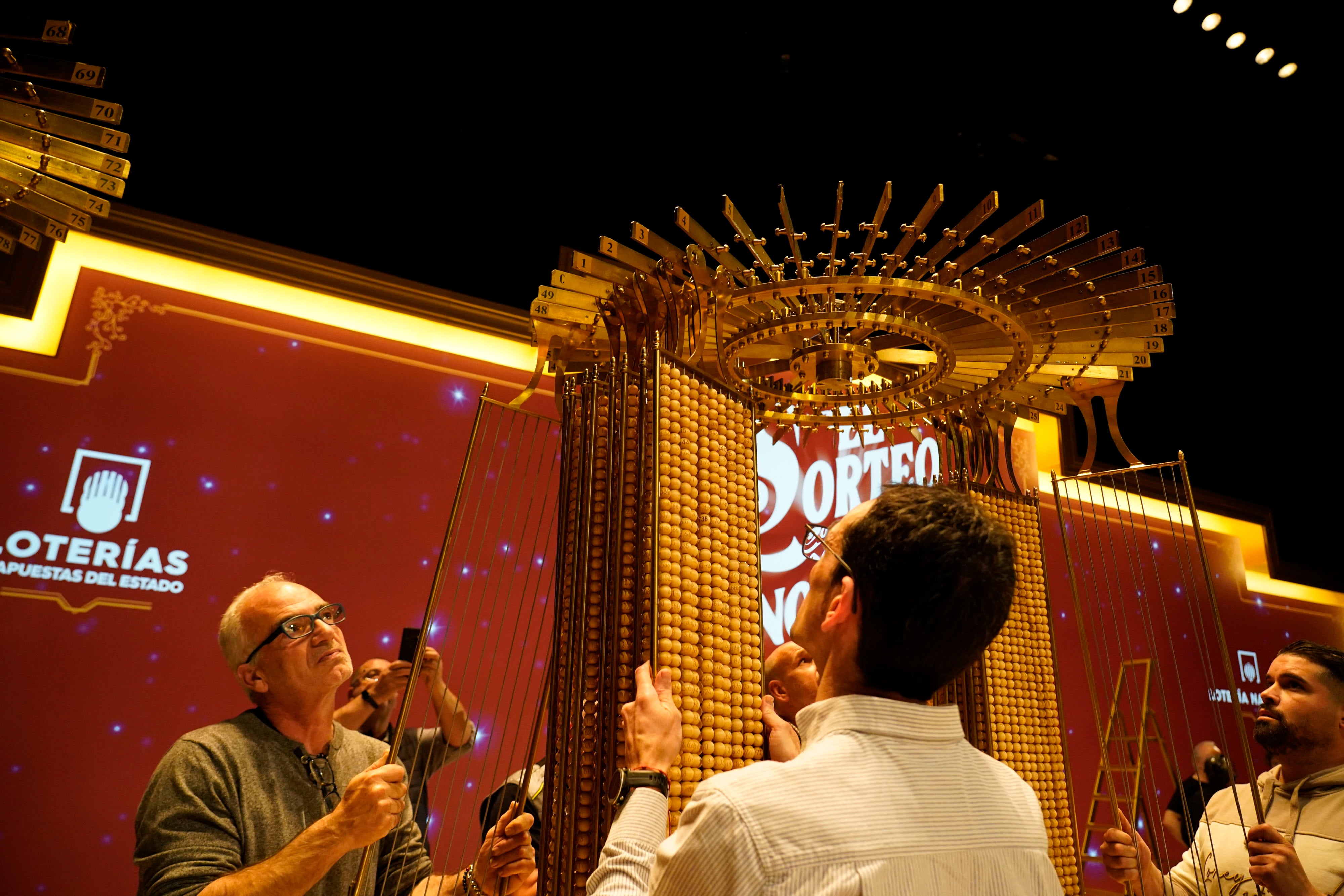 MADRID, 21/12/2025.- Personal de Loterías y Apuestas del Estado ha procedido a la cuelga en los paraguas de las liras que contienen las 100.000 bolas de números, dejando también preparadas las 1.807 bolas de premios que se utilizarán en el Sorteo de mañana. Terminada la cuelga, los claveros de Loterías y Apuestas del Estado han efectuado el cierre y precintado de las puertas del salón del Teatro Real. Miles de españoles estarán pendientes mañana lunes de lo que ya se ha convertido en toda una tradición, y en el pistoletazo de salida de estas fechas navideñas. El Sorteo Extraordinario de la Lotería de Navidad llenará de alegría e ilusión a numerosos hogares repartidos por toda la geografía. EFE/ Loterías Y Apuestas Del Estado SOLO USO EDITORIAL SOLO DISPONIBLE PARA ILUSTRAR LA NOTICIA QUE ACOMPAÑA (CRÉDITO OBLIGATORIO)