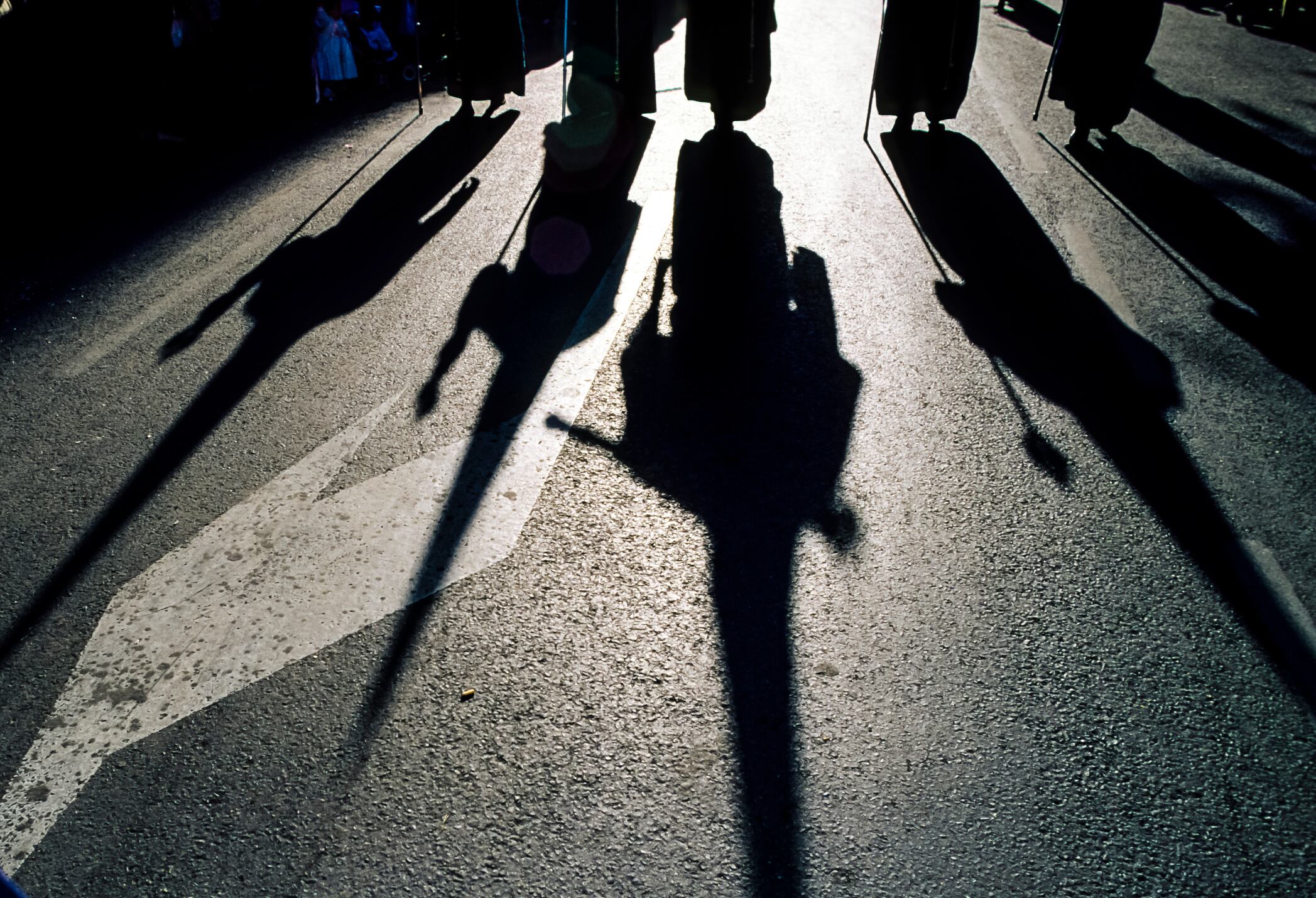 Sevilla, Spain - March 29, 1991: Shadows of hooded devotees marching on the Good Friday procession through the streets of the city.