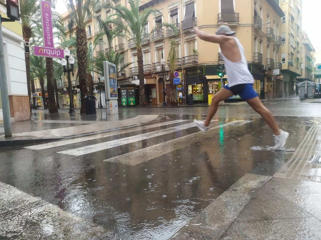 Un viandante intenta sortear un charco tras la lluvia caída a mediodía en la ciudad de Alicante.