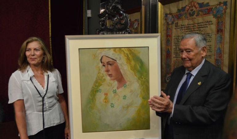 La pintora Reyes de la Lastra y el hermano mayor de La Macarena, Manuel García, escoltan el cartel del 50 aniversario de la Basílica