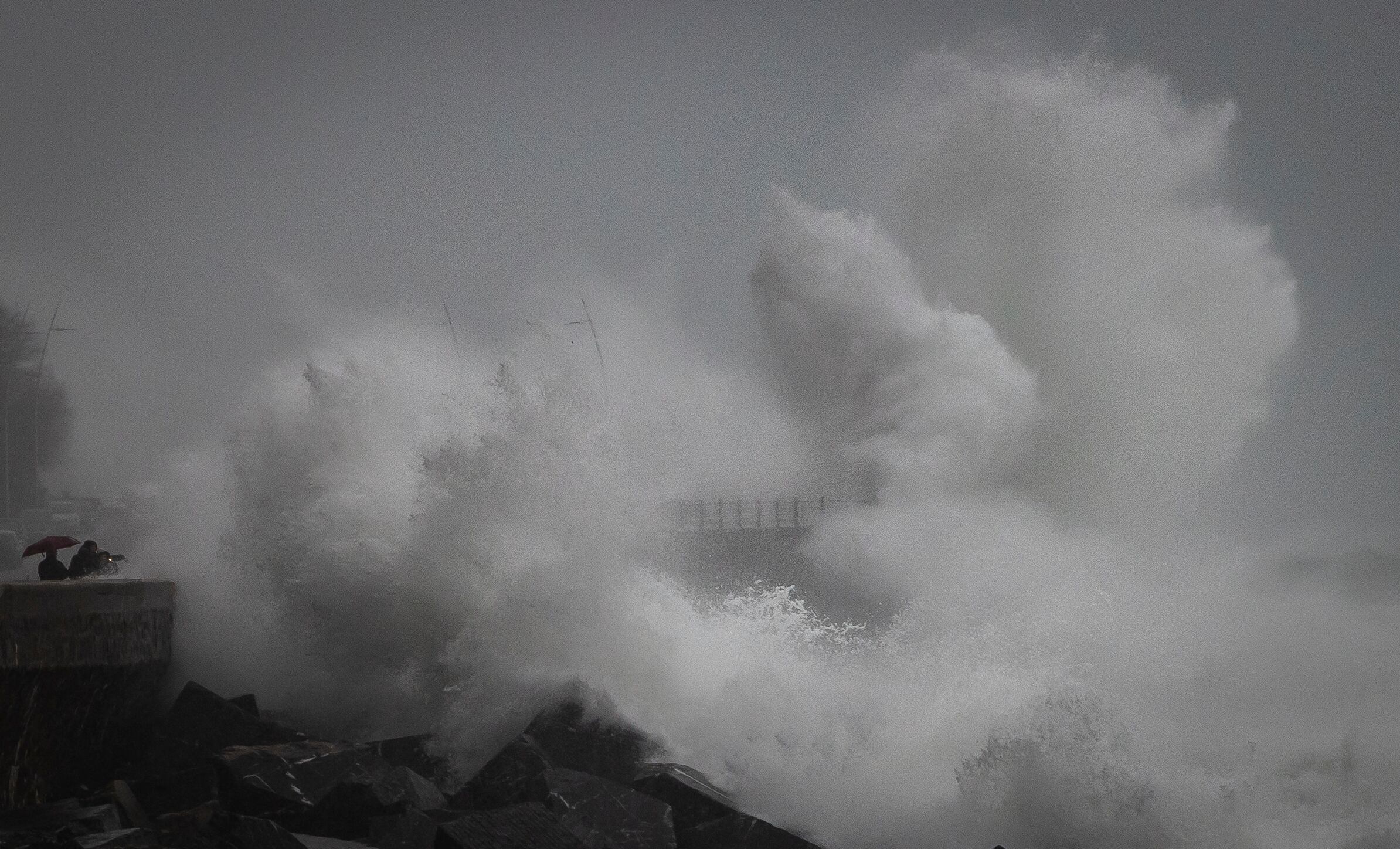 Varias personas observan el oleaje en el Paseo Nuevo de San Sebastián, donde se ha decretado la alerta naranja por impacto de olas en la costa