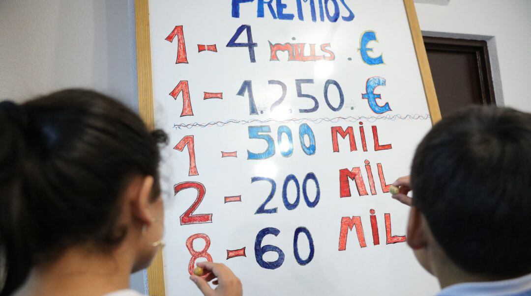 Dos niños de la residencia de San Ildefonso apuntan los premios del Sorteo de Navidad.