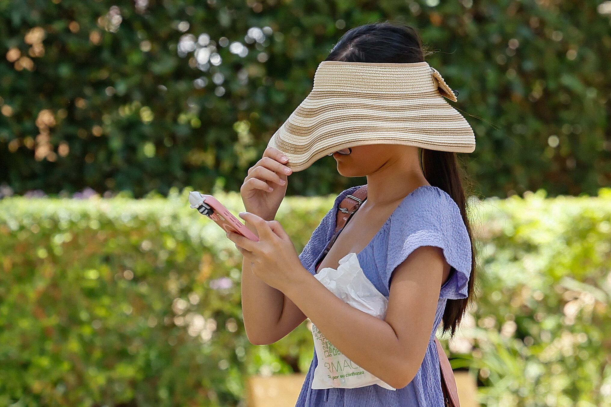 Una turista se tapa con un sombrero la cara para resguardarse del sol mientras camina por un parque en Sevilla. EFE /José Manuel Vidal