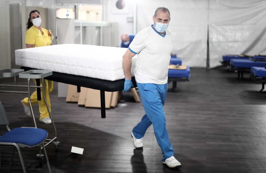 Dos profesionales sanitarios preparan camas para enfermos de coronavirus.