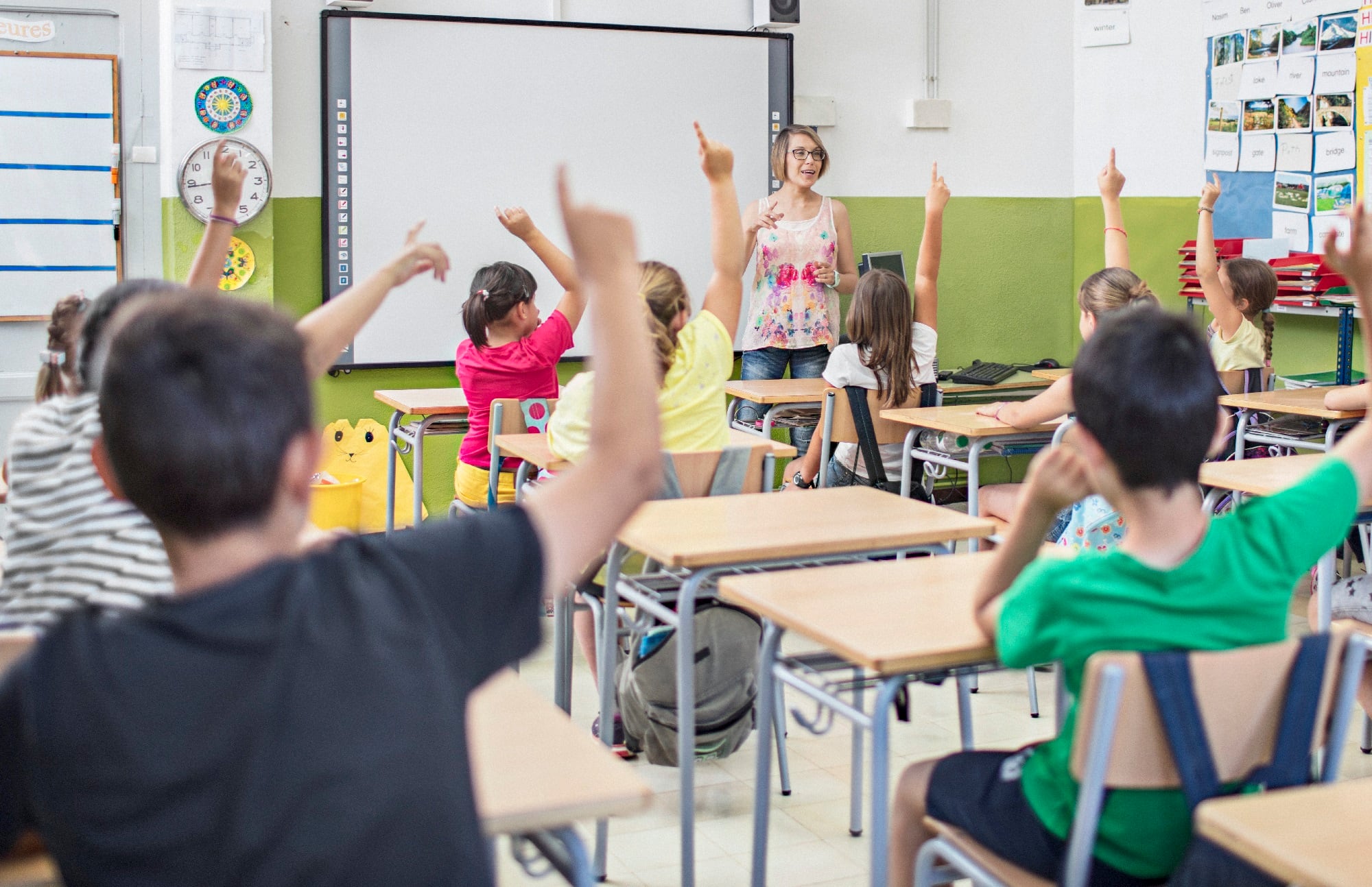 Niños y niñas levantan la mano en un aula de un Colegio