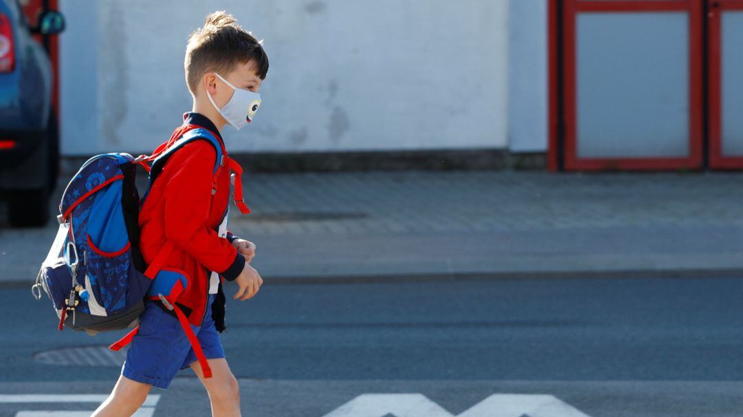 A child wearing a protective face mask walks a street as he arrives at a primary school