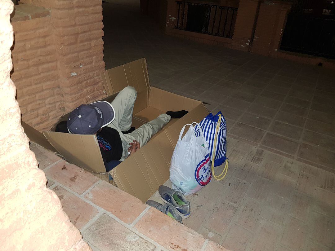 Brahim intenta acomodarse en una caja de cartón para pasar la noche en los Jardines de Puerta Oscura