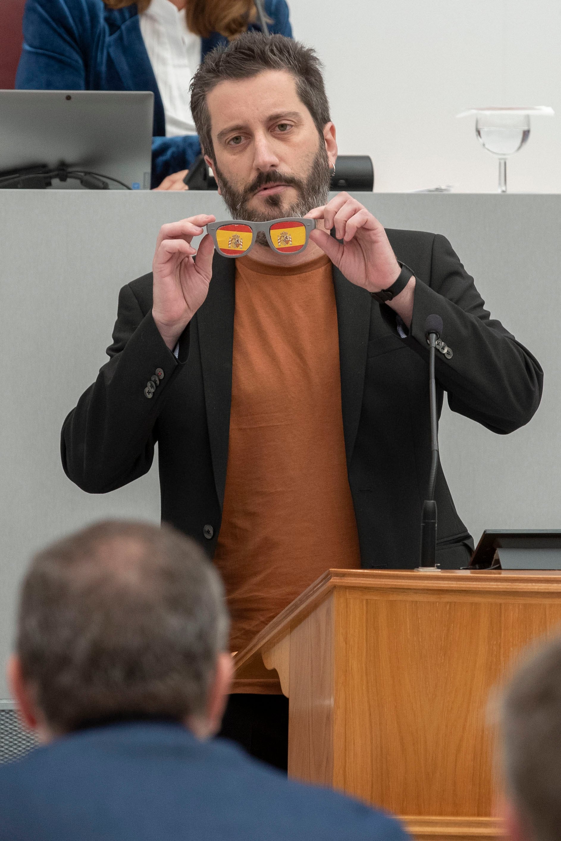 MURCIA, 22/11/2023.- El diputado de Podemos en el parlamento murciano Víctor Egío muestra unas gafas con la bandera de España durante un pleno de la Asamblea Regional de Murcia. EFE/Marcial Guilén
