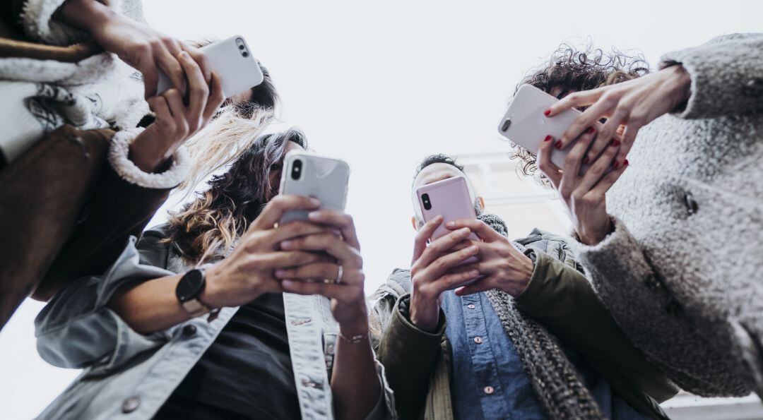 Varios jóvenes con su teléfono móvil.