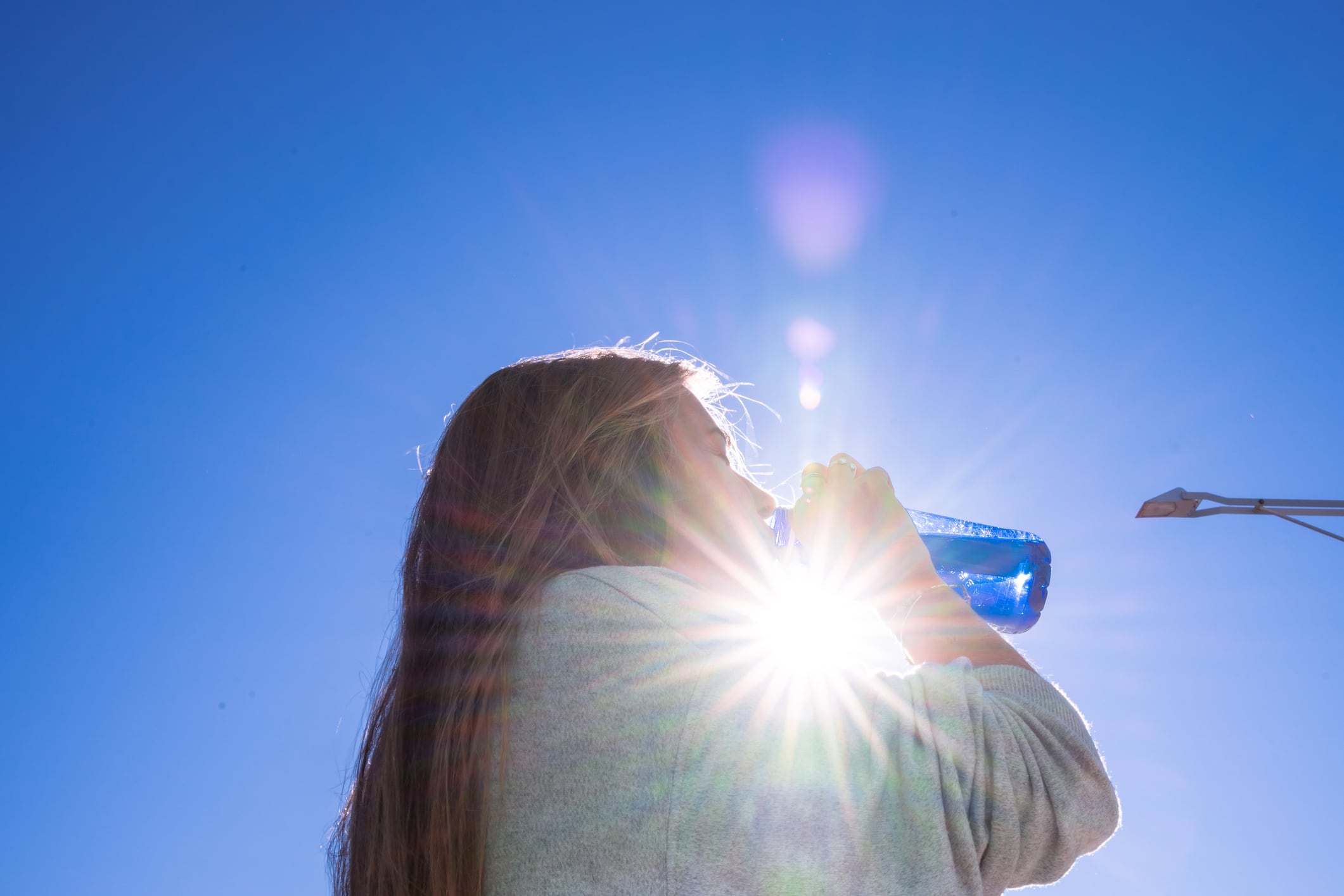 Una mujer bebe de una botella de agua mientras el sol le da en la cara.