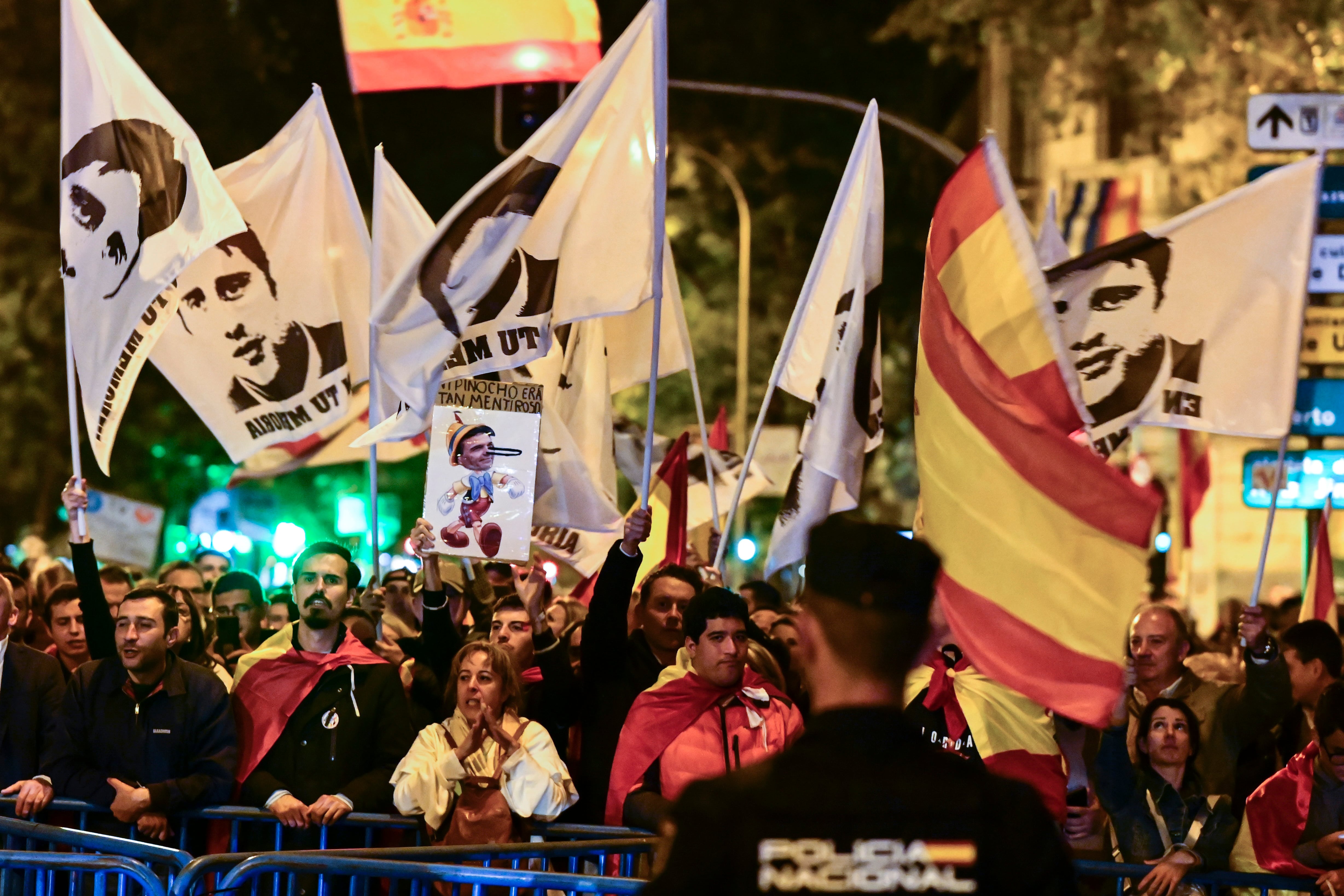 Unos jóvenes sostienen banderas de España y de Miguel Ángel Blanco, concejal de Ermua asesinado por ETA en 1997, frente a efectivos de la Policía durante la manifestación que han trasladado hasta las inmediaciones de La Moncloa y los accesos de la A-6 a la capital, este sábado.