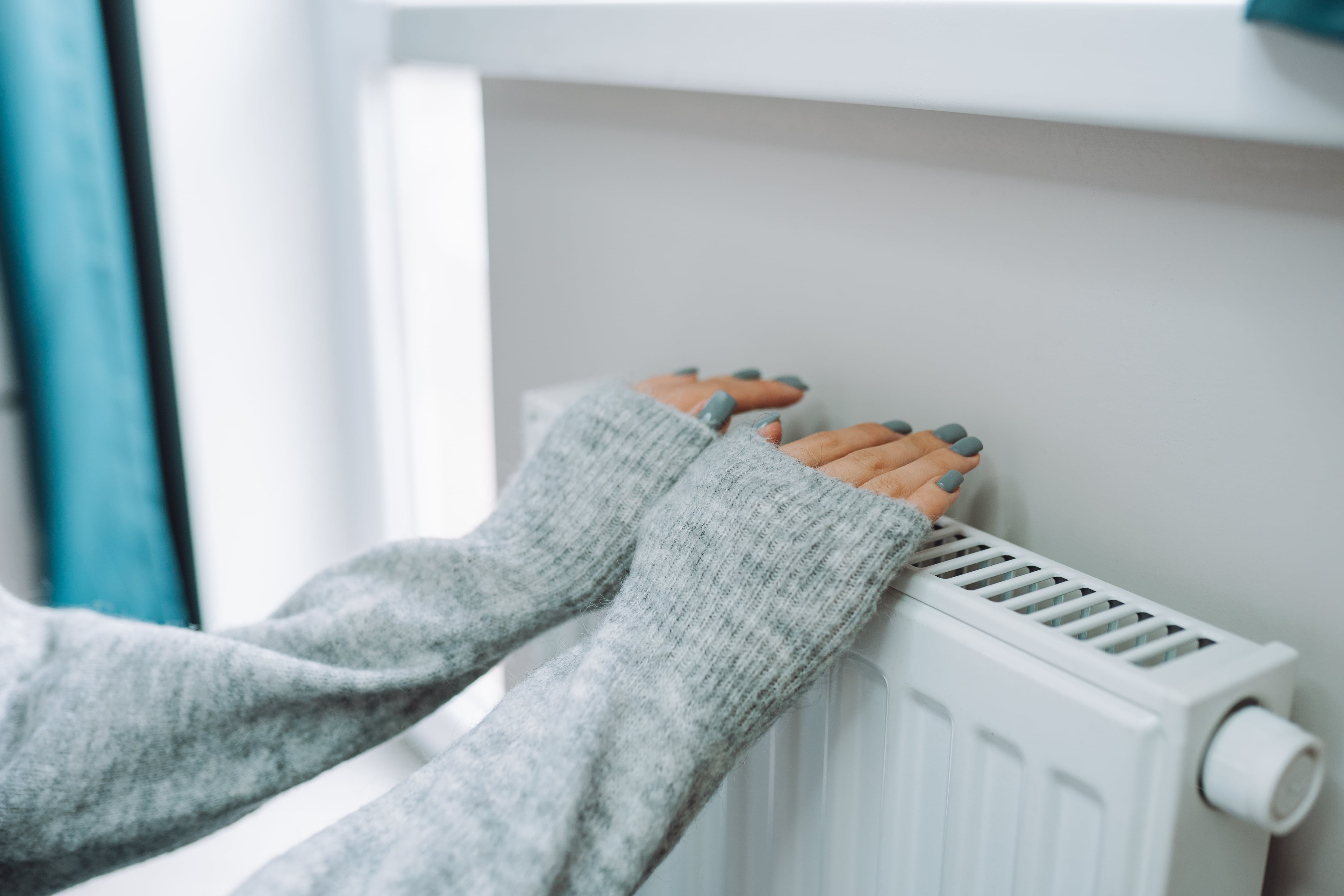 Una mujer se calienta las manos en el radiador