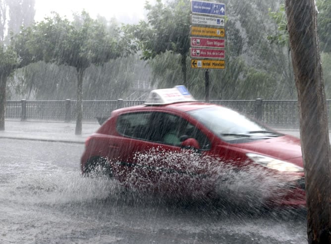 Un coche circula por la Avenida de Castilla, en Palencia, durante la tromba de agua y granizo, acompañada de aparato eléctrico, que se desencadenó este miércoles