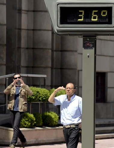 Dos hombres caminan junto un poste de temperatura en Ourense que marca 36 grados