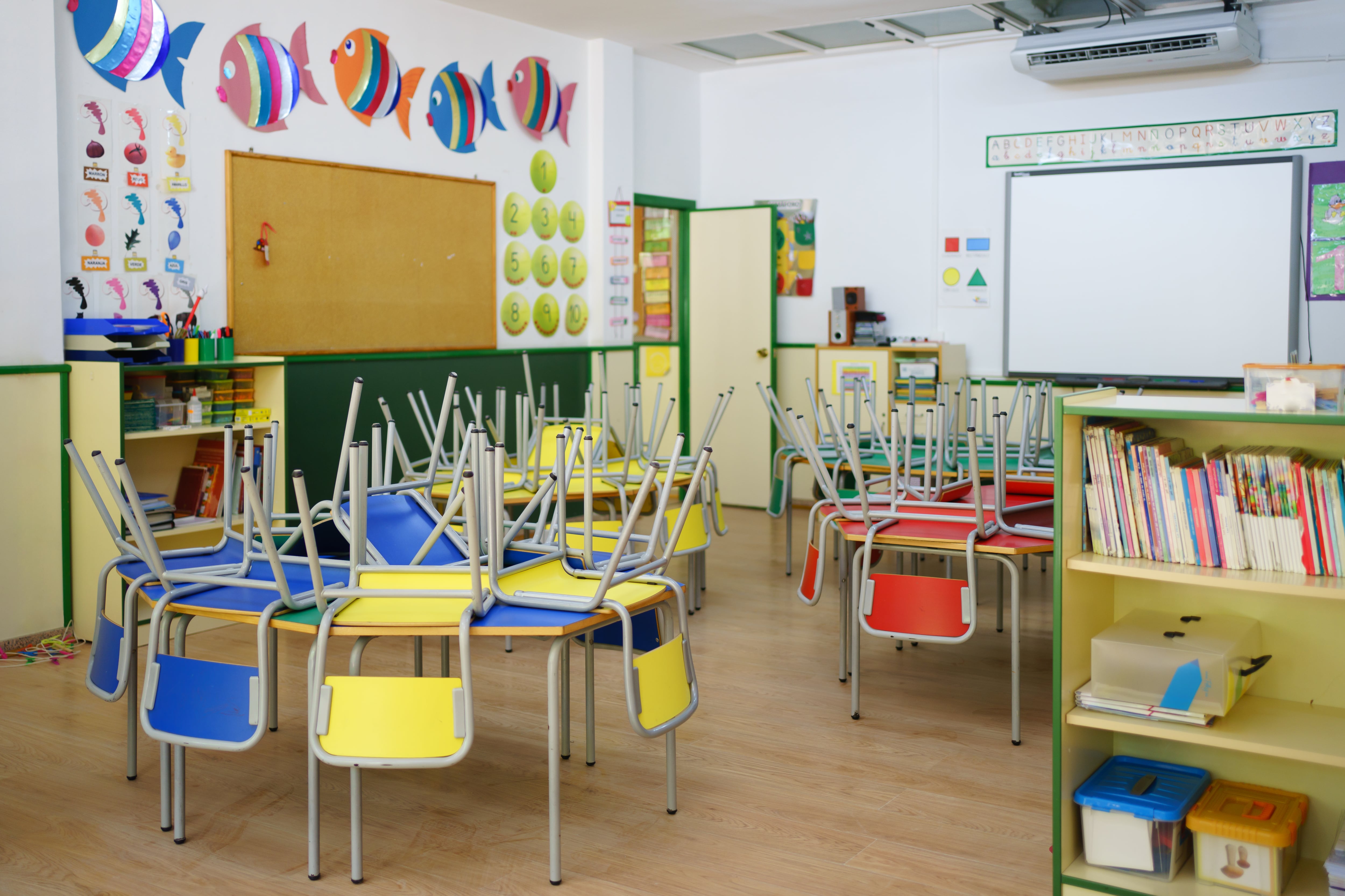 Wide view of a children&#039;s classroom at the school. Red, yellow and blue chairs arranged on the tables, white board and other school equipment.