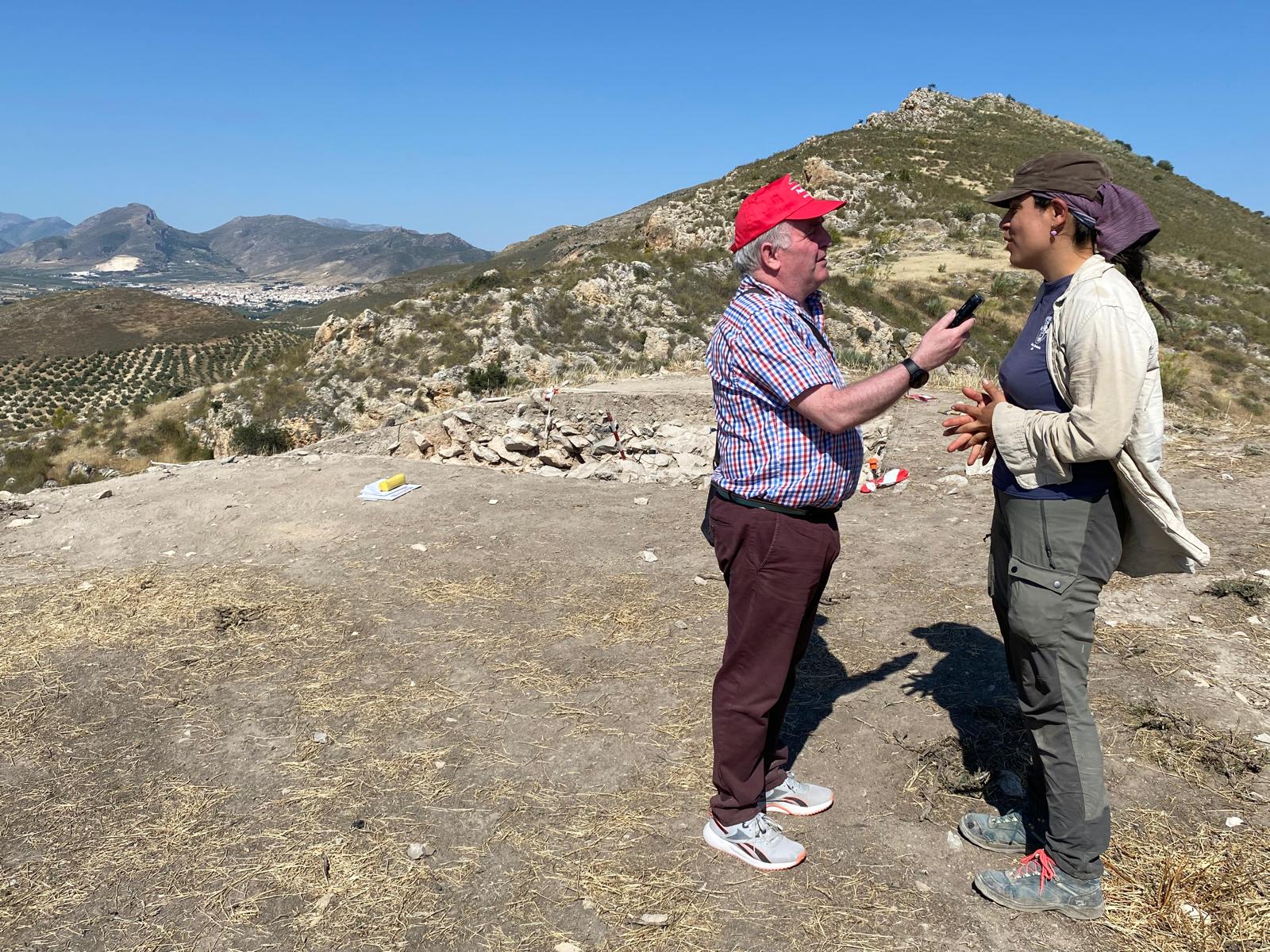 Momento de la entrevista a la doctorando Mercedes, Navero Rosales, sobre los trabajos en le yacimiento de El Fontanar, con el casco urbano de Jódar en el horizonte