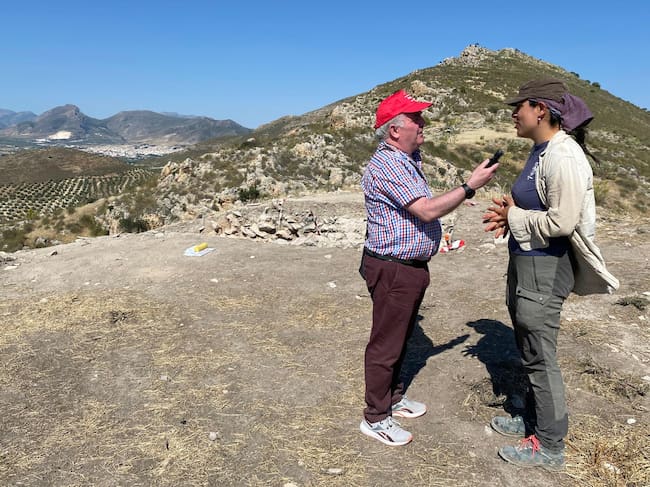 Momento de la entrevista a la doctorando Mercedes, Navero Rosales, sobre los trabajos en le yacimiento de El Fontanar, con el casco urbano de Jódar en el horizonte