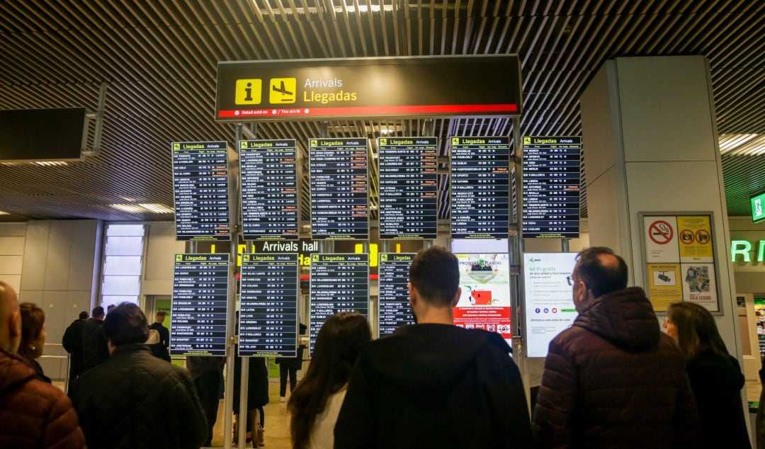 Varios usuarios consultan el panel de llegadas en Barajas.