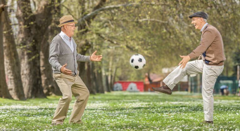 Dos hombres mayores juegan al fútbol en un parque. 