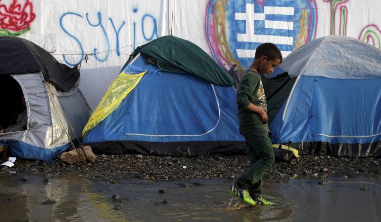 Un niño camina en un charco al lado de tiendas de campaña en un campamento improvisado para los refugiados en la frontera entre Grecia y Macedonia