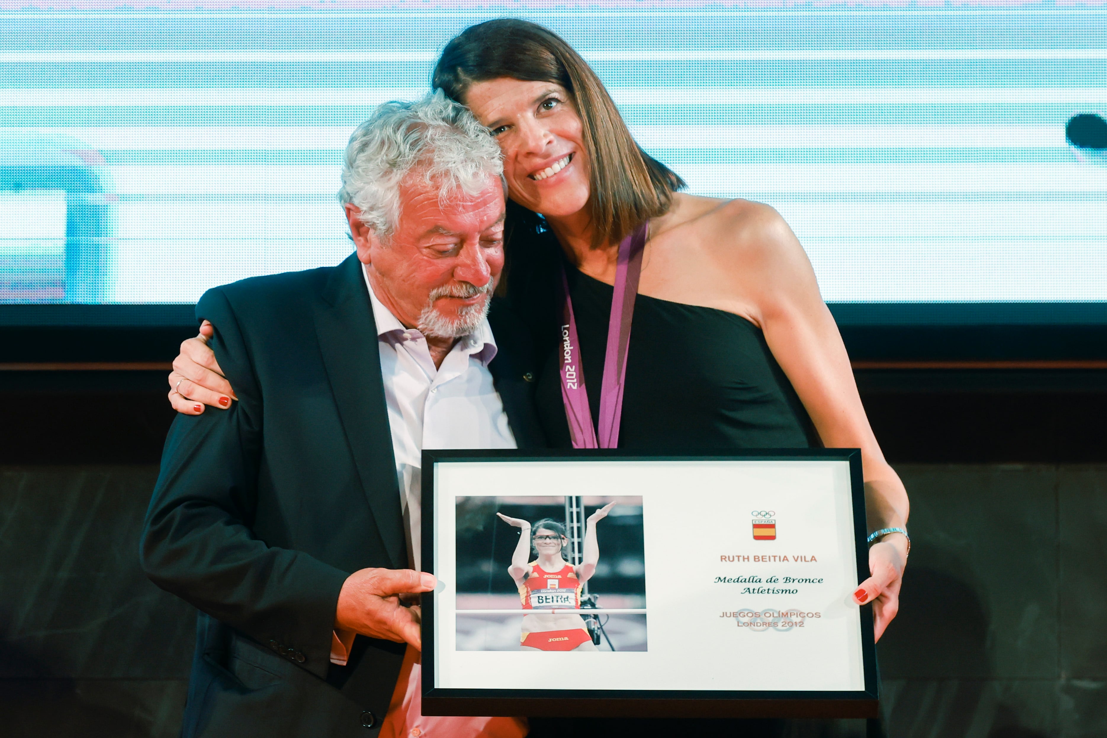 La saltadora santanderina Ruth Beitia recibe la medalla de bronce de salto de altura de los Juegos de Londres 2012, que le fue adjudicada nueve años después, en 2021, tras la descalificación por dopaje de la rusa Svetlana Shkolina, este lunes en la sede del Comité Olímpico Español (COE). Junto a ella, Ramón Torralbo, su entrenador. EFE/ Javier Lizon