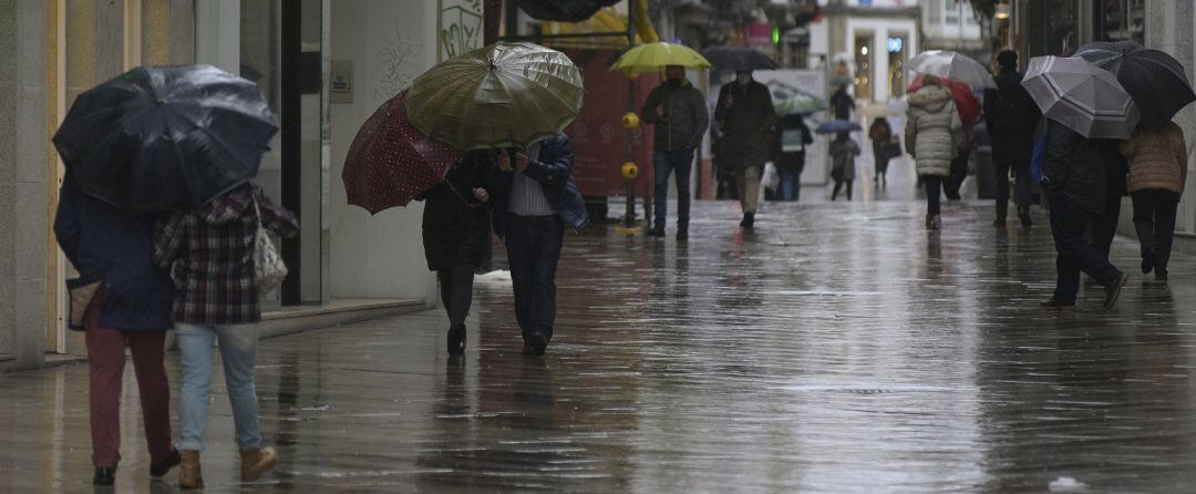 Transeúntes caminan protegidos por una vía de A Coruña