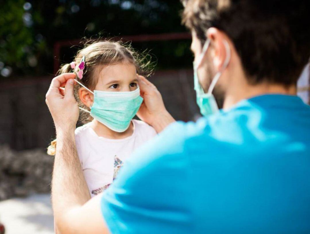 Un padre colocando una mascarilla a su hija