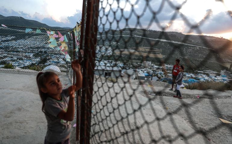 Una niña juega con la verja de un campamento de refugiados en Siria.