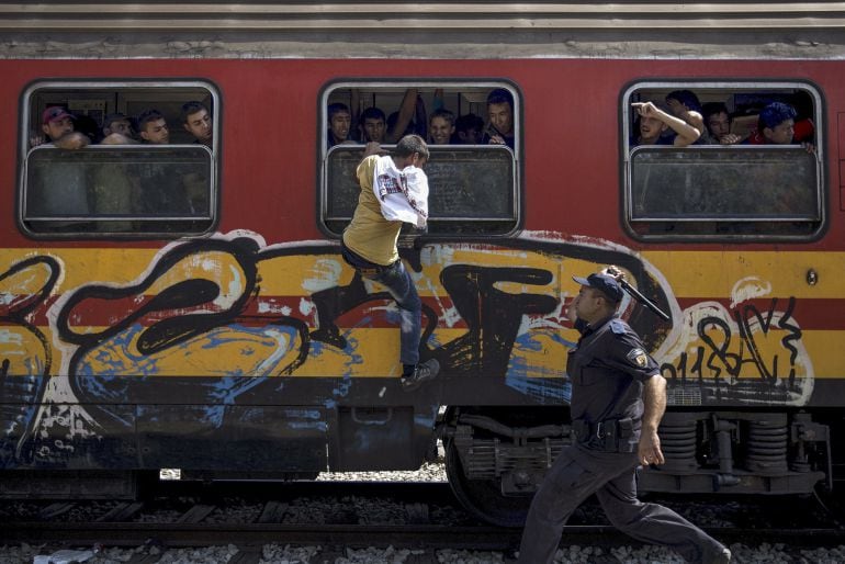 Un policía intenta impedir que un joven migrante suba a un tren en una estación de Macedonia