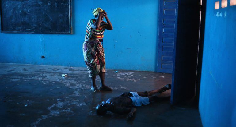 MONROVIA, LIBERIA - AUGUST 15:  Umu Fambulle stands over her husband Ibrahim after he staggered and fell, knocking him unconscious in an Ebola ward on August 15, 2014 in Monrovia, Liberia. People suspected of contracting the Ebola virus are being sent by 