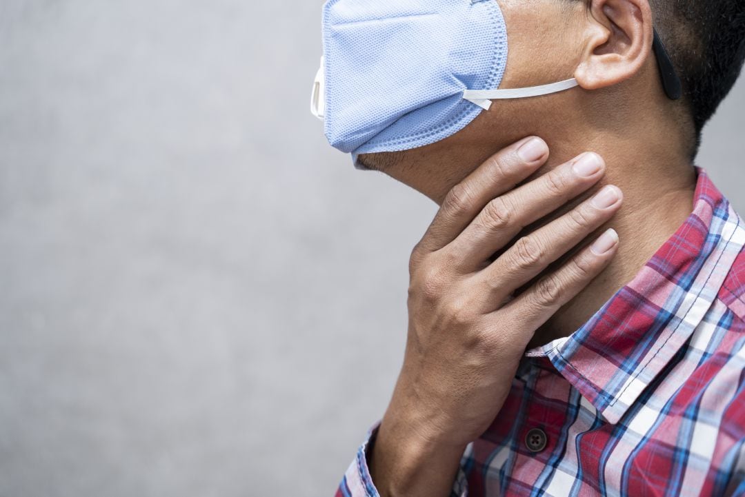 Un hombre con mascarilla se toca el cuello ante un posible dolor de garganta