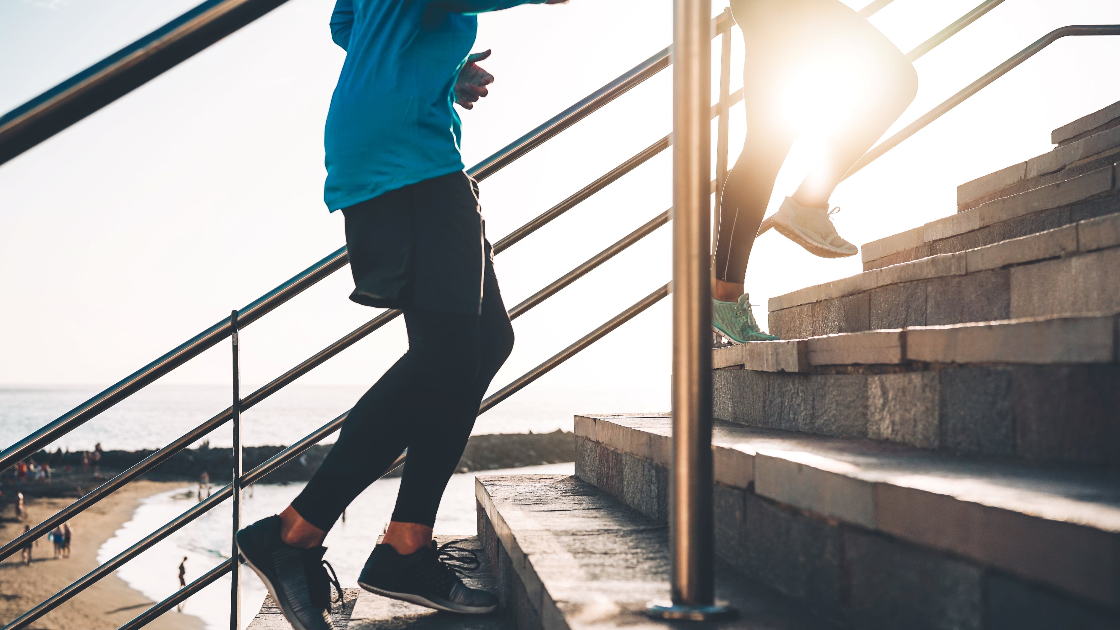 View of runners legs training outdoor - Young couple doing a workout session on stairs next the beach at sunset - Healthy people, jogging and sport lifestyle concept