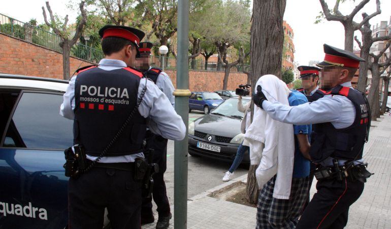 Quatre agents dels Mossos d'Esquadra amb el detingut, amb la cara tapada amb una jaqueta divendres.
