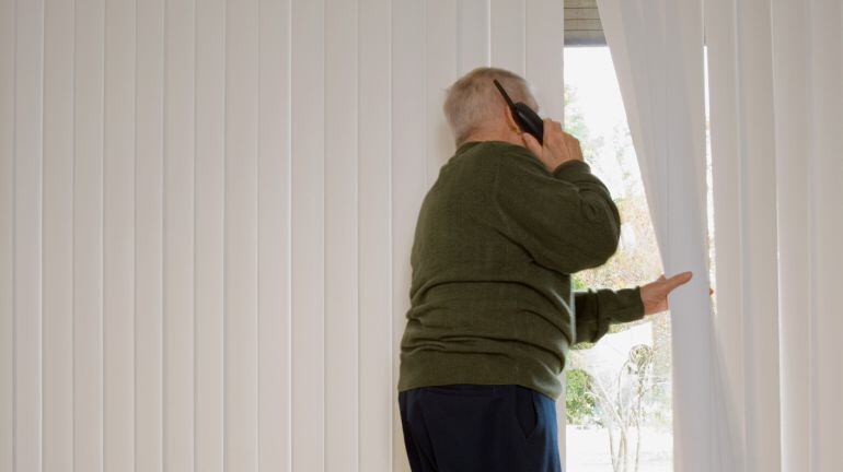 Un anciano mirando por la ventana de su casa. 