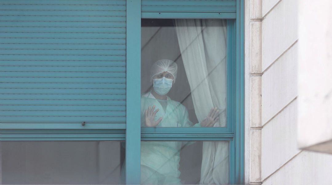 Una trabajadora del personal sanitario protegida con mascarilla se asoma por una de las ventanas de una residencia.