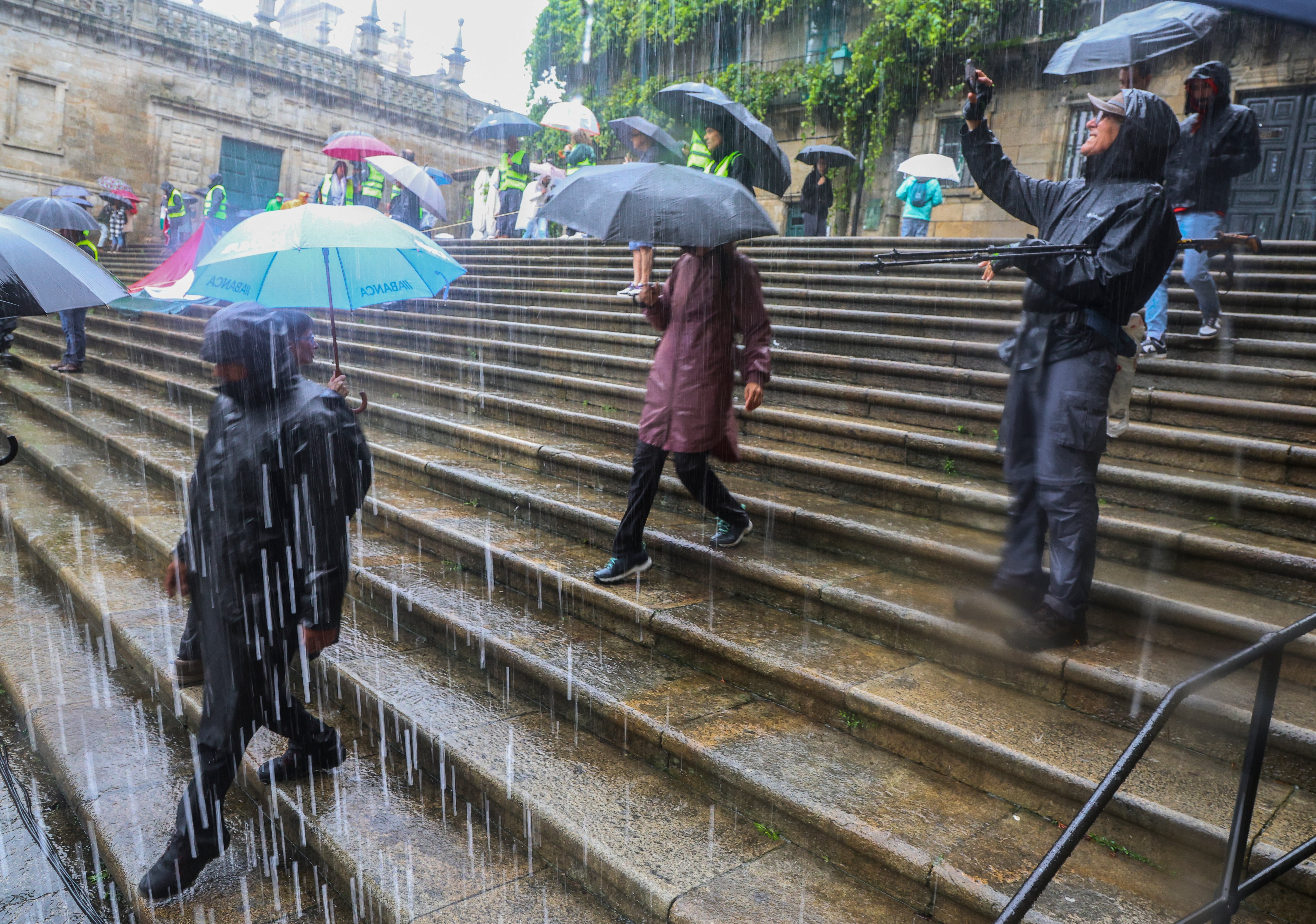 Turistas y peregrinos intentan protegerse de fuertes precipitaciones en la compostelana Plaza de la Quintana (Santiago)