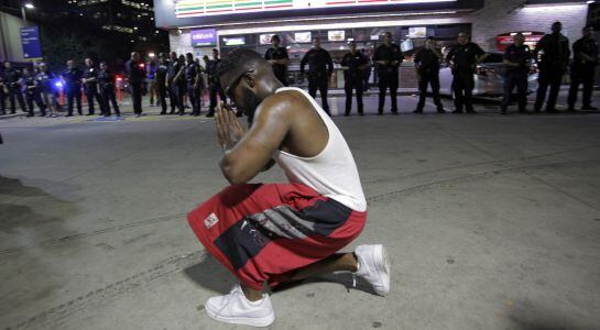 Un joven se arrodilla frente a los policías desplegados durante una manifestación contra la violencia policial hacia los negros en EEUU.