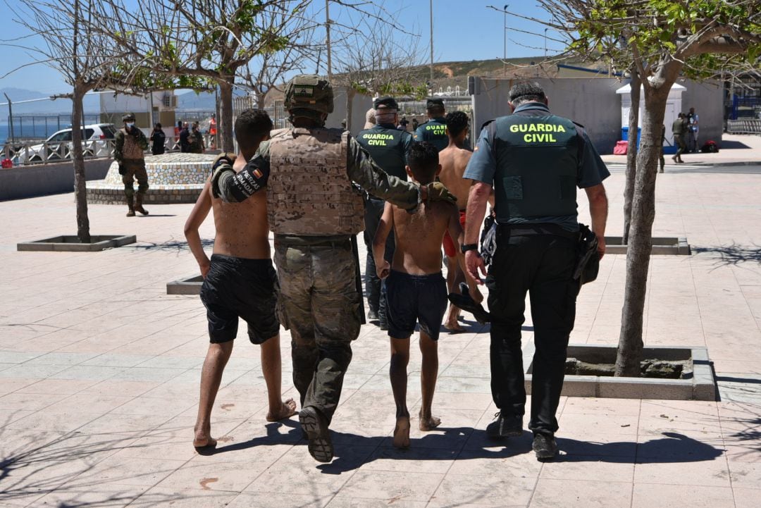 Un militar del ejército español y un agente de la Guardia Civil ayudan a dos menores migrantes procedentes de Marruecos a su llegada a Ceuta 