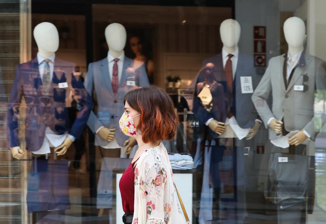 Una mujer protegida con mascarilla pasa junto a una tienda de trajes 