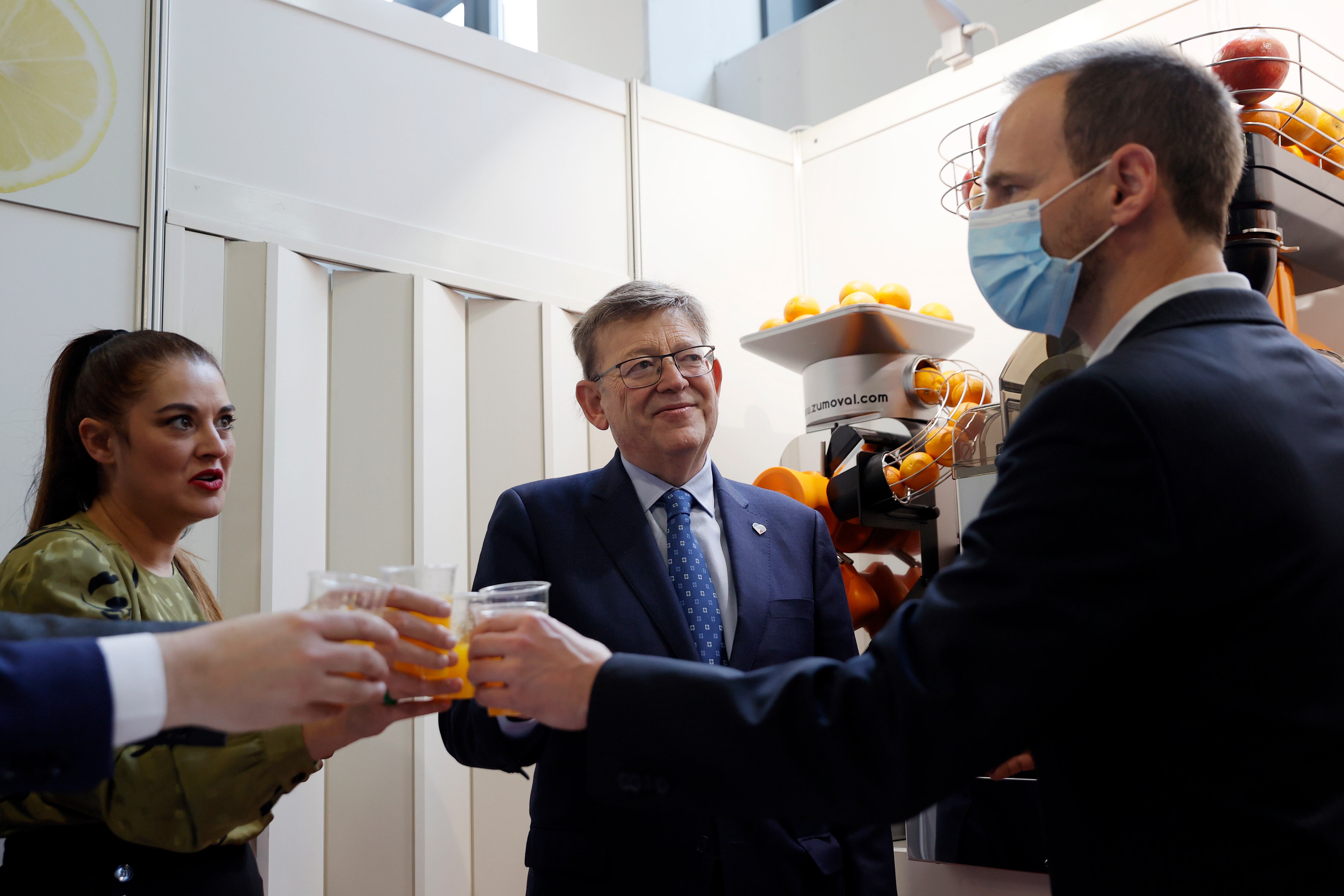 El president de la Generalitat, Ximo Puig (c), y la consellera de Agricultura, Desarrollo Rural, Emergencia Climática y Transición Ecológica, Mireia Mollà, brindan con zumo de naranja en un stand de una de las empresas de la Comunitat Valenciana que participan en el certamen alemán, Fruit Logistica. EFE/Juan Carlos Cárdenas