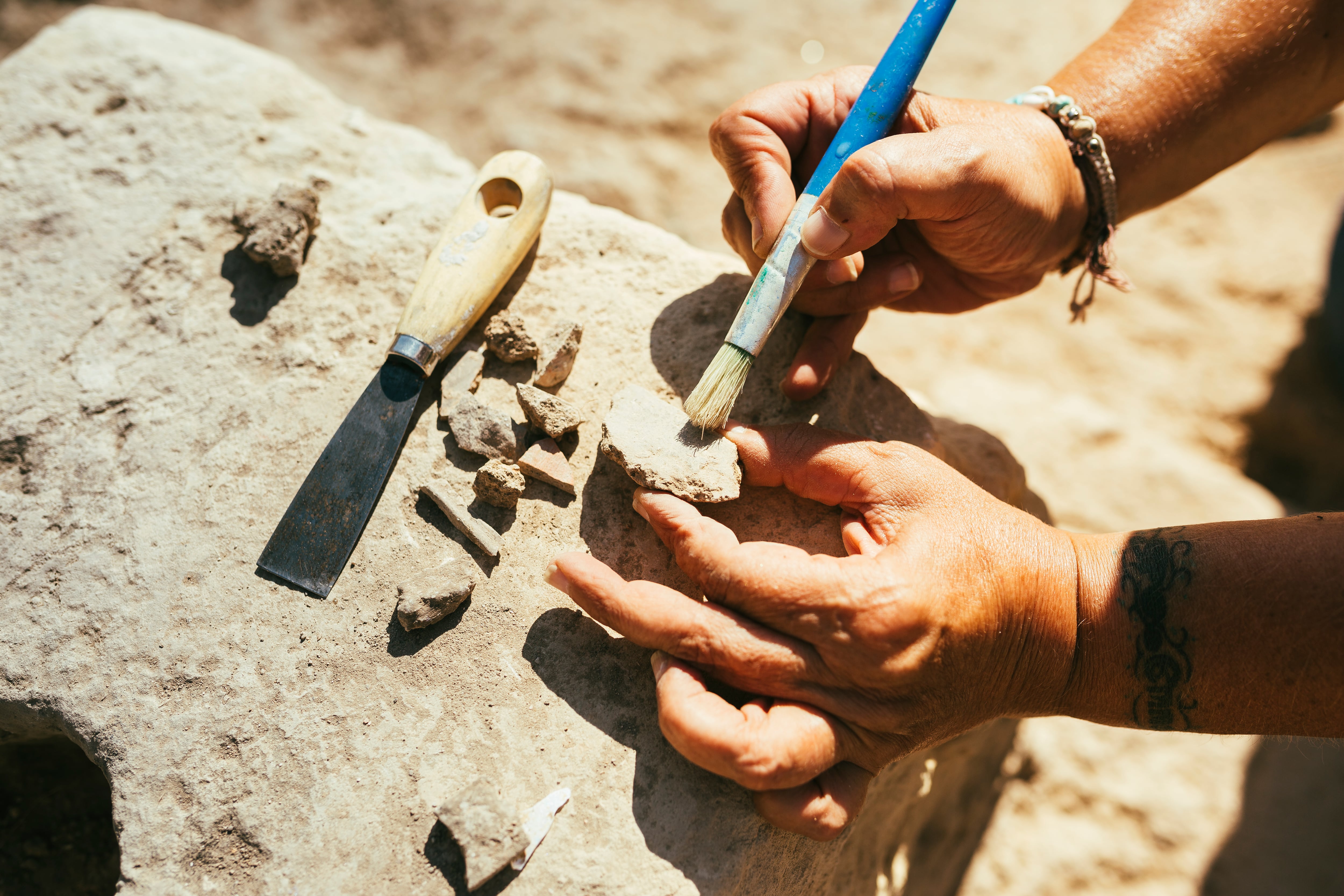 Woman's hands using a brush to clean up a piece of ancient pottery on an archaeological site