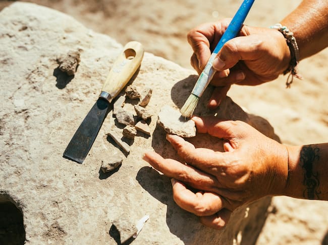 Woman's hands using a brush to clean up a piece of ancient pottery on an archaeological site